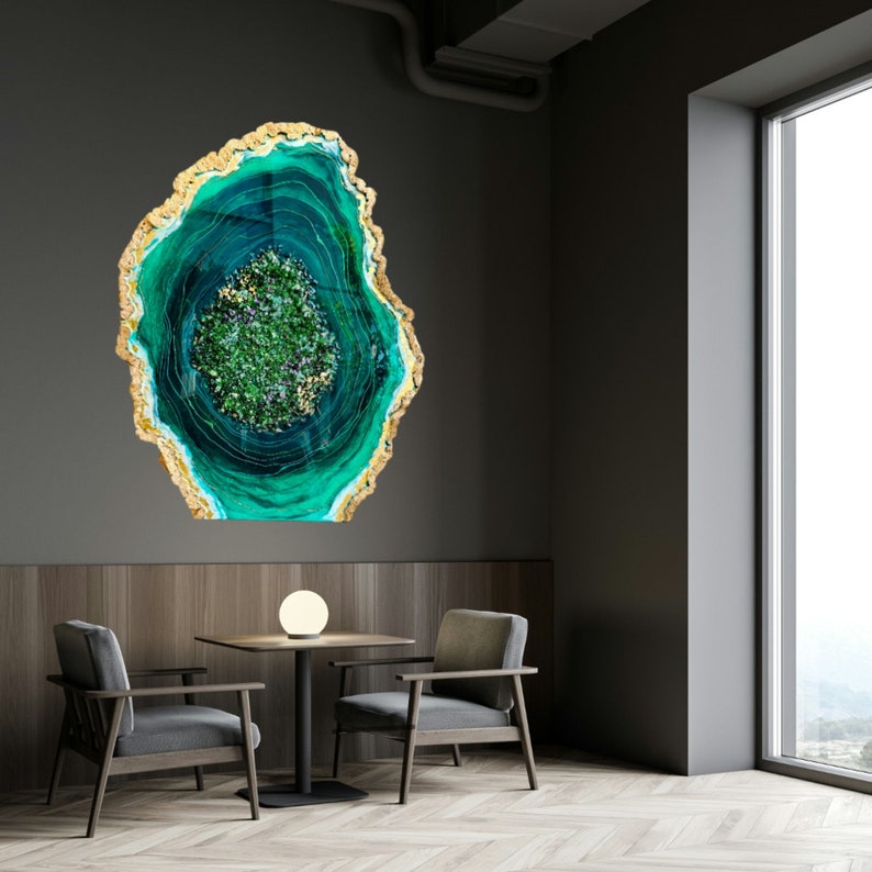May include: A green and gold agate wall art piece with a swirling pattern. The art is hanging on a gray wall in a room with two chairs and a table.