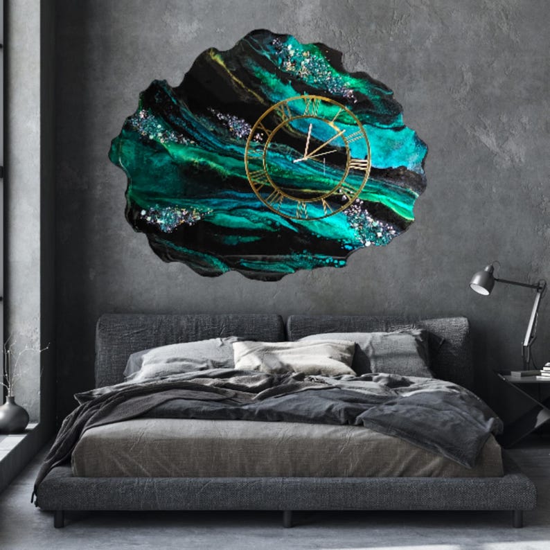 May include: A large, abstract wall clock with a gold-colored frame and Roman numerals. The clock face is set against a swirling background of teal, black, and green resin with glitter accents. The clock is mounted on a gray wall above a bed.