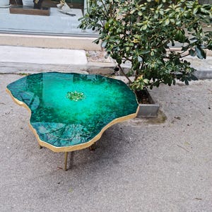 Könnte beinhalten: Ein grüner Couchtisch aus Harz mit einer goldenen Blattverkleidung und einem goldenen Metallgestell. Die Tischplatte ist in Form eines großen, unregelmäßigen Steins geformt.