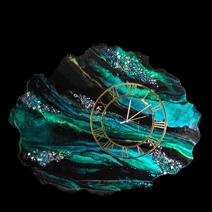 May include: A decorative wall clock with a gold-colored frame and Roman numerals. The clock is set on a unique, irregularly shaped base with a swirling pattern of black, teal, and gold colors. The base has a glossy finish and is embellished with glitter.
