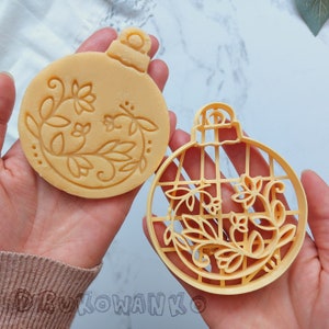 Può includere: Due tagliabiscotti in plastica gialla a forma di ornamenti natalizi. Un tagliabiscotti presenta un motivo floreale e l'altro un motivo geometrico.