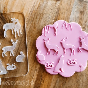 May include: A pink silicone mold with raised images of deer, rabbits, snakes, and a wolf. The mold is shaped like a cloud and has a smooth, glossy finish.