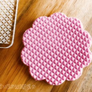 Pode incluir: Forma de fondant de silicone rosa com padrão de waffle. A forma tem o formato de uma flor com bordas arredondadas.