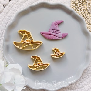 Peut inclure: Quatre emportes-pièces en forme de chapeau de sorcière sur une assiette grise. Trois sont jaunes et un est violet.