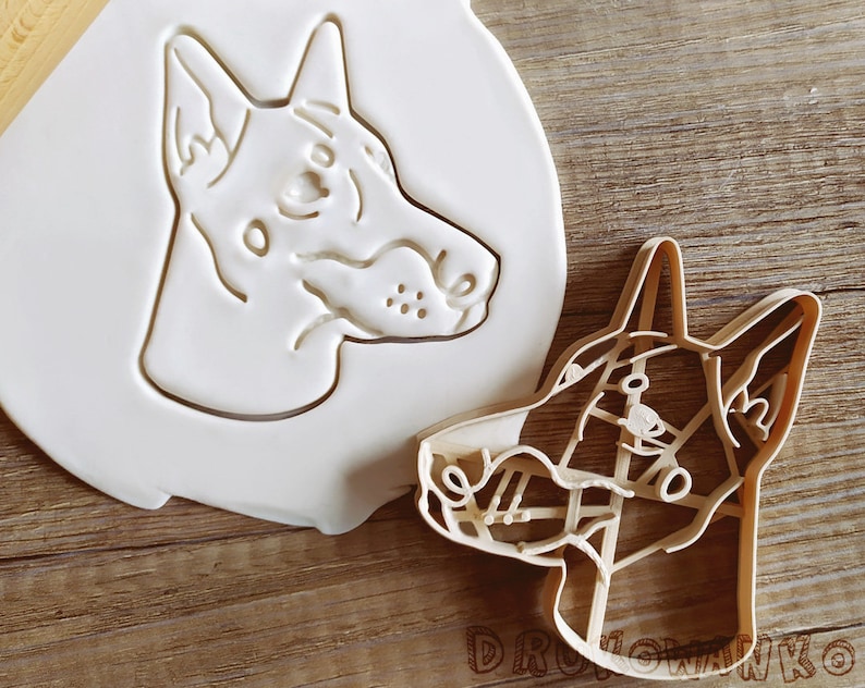 K&ouml;nnte beinhalten: Ein wei&szlig;er Plastik-Ausstecher in Form eines Hunde Kopfes. Daneben liegt ein h&ouml;lzerner Ausstecher in Form eines Hunde Kopfes.