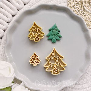 May include: Four Christmas tree cookie cutters, two are gold and two are green. The cutters are on a gray plate.