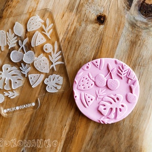 Può includere: Due stampi in silicone rosa per la cottura. Uno stampo è trasparente e mostra un disegno di vari frutti e foglie. L'altro stampo è rosa e mostra un disegno di vari frutti e foglie. Gli stampi sono su una superficie di legno. Il testo "DRUKOWANKO" è sullo stampo trasparente.