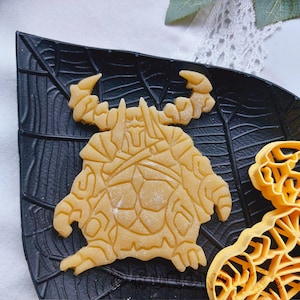 May include: A detailed cookie cutter in the shape of a fantasy creature with a helmet and armor. The cutter is made of a light brown dough and is sitting on a black surface.