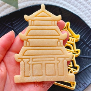 Puede incluir: Un cortador de galletas de color marrón claro con forma de pagoda china tradicional con un diseño detallado. El cortador está hecho de plástico y está listo para ser utilizado para crear deliciosas galletas.