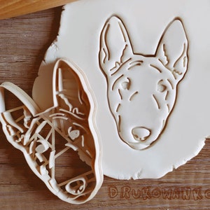 May include: A white plastic cookie cutter in the shape of a Bull Terrier dog's head. The cutter is on a white surface.