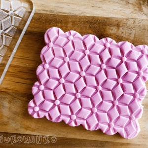 May include: A pink silicone baking stamp with a geometric pattern of diamonds and circles. The stamp is on a wooden surface.