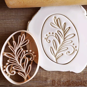 Puede incluir: Un primer plano de un cortador de galletas con forma ovalada con un diseño floral. El cortador está hecho de plástico y es de color marrón. El cortador está sobre una superficie blanca.