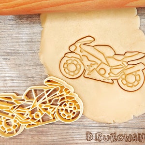 Peut inclure: Un emporte-pièce en plastique en forme de moto. L'emporte-pièce est sur une surface en bois à côté d'une pâte.