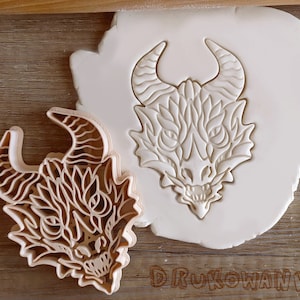 Puede incluir: Dos cortadores de galletas de dragón detallados, uno con un diseño más intrincado y el otro con un diseño más simple. Ambos están hechos de plástico marrón claro.