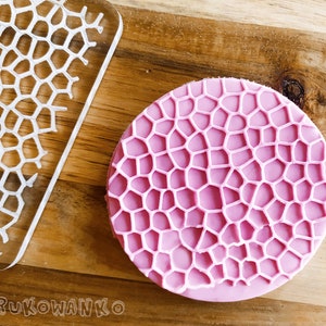 May include: A pink silicone mold with a raised honeycomb pattern. The mold is round and has a smooth surface.