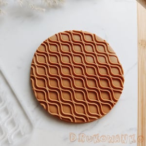 Può includere: Un tappetino da forno rotondo in silicone marrone con un motivo a griglia ondulata. Il tappetino è progettato per l'uso con fondant, pasta di gomma e altre decorazioni commestibili.