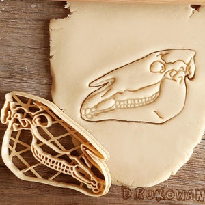 May include: A close-up of a cookie cutter in the shape of a horse skull. The cutter is made of plastic and has a detailed design. The cutter is on top of a piece of cookie dough.