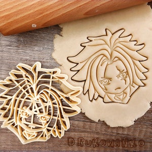 Può includere: Due stampini per biscotti a forma di un personaggio dei cartoni animati con i capelli a punta. Gli stampini per biscotti sono in metallo dorato e sono su una superficie di legno.