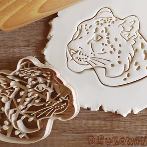 Può includere: Due stampini per biscotti a forma di testa di leopardo. Gli stampini sono in plastica bianca e sono su una superficie di legno.
