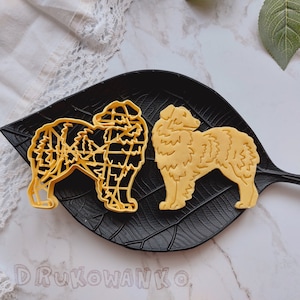 Könnte beinhalten: Zwei gelbe Plastik-Ausstecher in Form von Hunden. Die Ausstecher befinden sich auf einem schwarzen, blattartigen Teller.