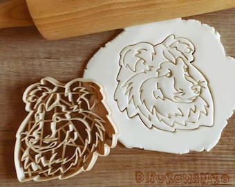 May include: Two cookie cutters in the shape of a dog's head. The cutter on the left is detailed with a patterned design. The cutter on the right is a simple outline of a dog's head.