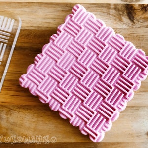 May include: A pink silicone embossing mat with a geometric pattern. The mat has a scalloped edge.