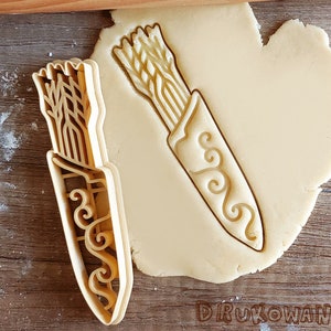 May include: A cookie cutter set featuring two designs: a quiver of arrows and a single arrow. The cutters are made of a light brown plastic and have a detailed design.