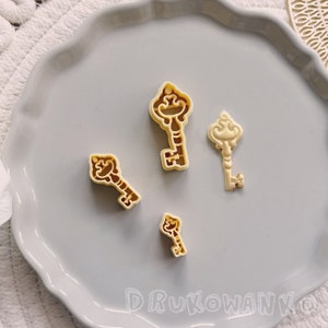 以下が含まれることがあります： 薄い灰色の皿の上に、プラスチック製の鍵の形をしたクッキーカッターが4つあります。カッターはさまざまなサイズで、ヴィンテージスタイルです。
