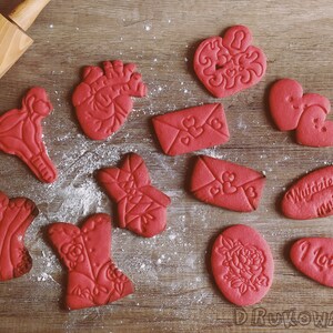 May include: A collection of red sugar cookies decorated with various Valentine's Day themes, including hearts, flowers, anatomical hearts, and the words "I Love You" and "Wyglądasz za mnie".
