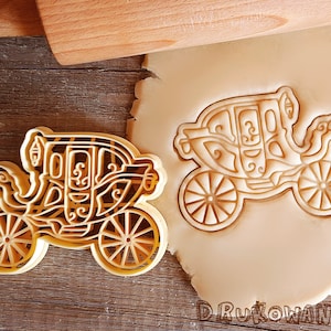 K&ouml;nnte beinhalten: Ein goldfarbener Keksausstecher in Form einer Kutsche. Der Ausstecher ist mit filigranen Designs verziert und hat vier R&auml;der.