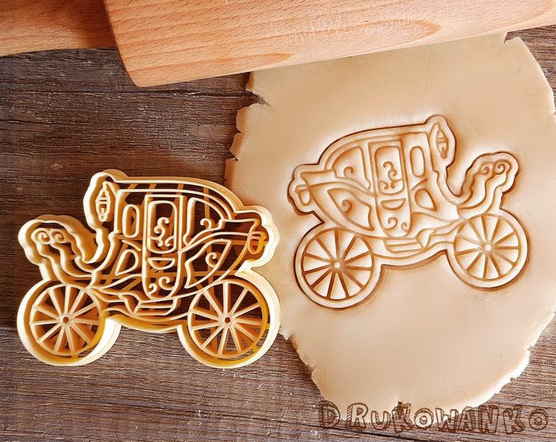 K&ouml;nnte beinhalten: Ein goldfarbener Keksausstecher in Form einer Kutsche. Der Ausstecher ist mit filigranen Designs verziert und hat vier R&auml;der.