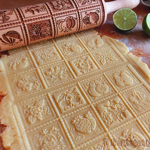 May include: A wooden rolling pin with a decorative design of various fruits and flowers. The rolling pin is used to create patterned impressions in a sheet of dough.