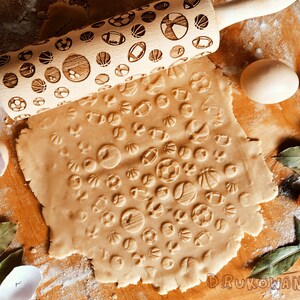 May include: A wooden rolling pin with a sports ball design is used to roll out dough for cookies. The dough is covered in impressions of various sports balls, including basketballs, footballs, and soccer balls.