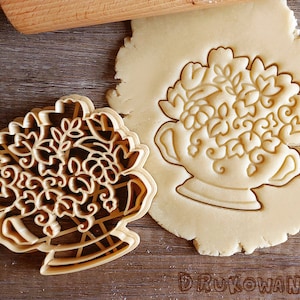Può includere: Un tagliapasta dorato a forma di bouquet di fiori in un vaso. Il tagliapasta è mostrato sopra un impasto per biscotti semplice.