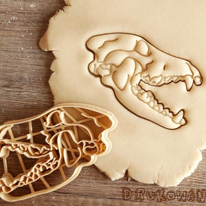 Puede incluir: Un primer plano de un cortador de galletas con forma de cráneo de animal. El cortador está hecho de plástico y es de color beige. El cortador está sobre una masa.