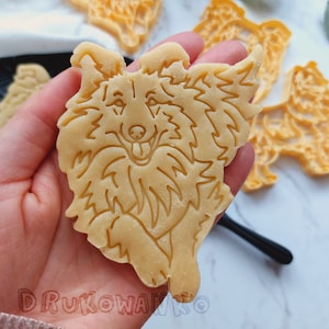 May include: A cookie cutter in the shape of a dog, made from light brown dough. The dog is running and has a happy expression on its face.