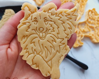 May include: A cookie cutter in the shape of a dog, made of light brown dough. The dog is running and has a happy expression on its face.