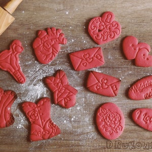 May include: A collection of red sugar cookies decorated with various Valentine's Day themes, including hearts, flowers, anatomical hearts, and the words "I Love You" and "Wyglądasz za mnie".