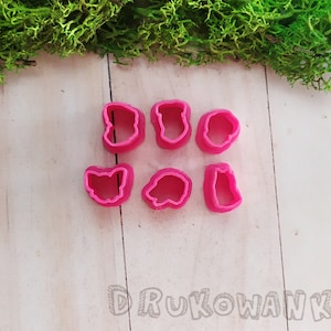 Op de afbeelding: Set van zes roze plastic koekjesvormen in de vorm van een kat, een beer, een fles, een bloem, een hart en een paddenstoel.