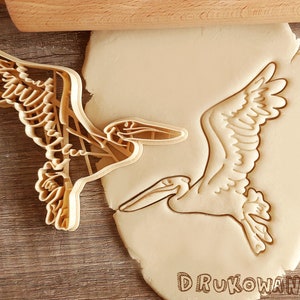 May include: A cookie cutter in the shape of a pelican. The cutter is made of metal and has a detailed design. The cutter is shown on top of a piece of cookie dough.