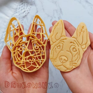 Könnte beinhalten: Ein gelber Ausstecher in Form eines Hundekopfes neben einem Hundekeks. Der Ausstecher hat ein detailliertes, offenes Design. Der Keks ist hellbraun mit detaillierten Gesichtszügen. Der Text "DRUKOWANKO" ist sichtbar.