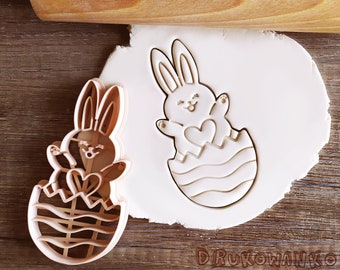 May include: Two cookie cutters shaped like bunnies holding hearts inside of eggs. The cutters are made of a light brown plastic.