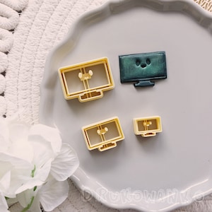 May include: Four plastic cookie cutters shaped like televisions. The cutters are yellow and have a green television with a cartoon face.