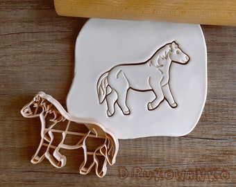 May include: A white plastic cookie cutter in the shape of a horse, next to a brown wooden rolling pin and a smaller, brown plastic cookie cutter in the shape of a horse.