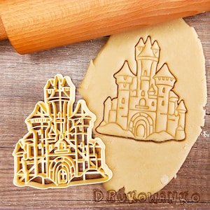 May include: A cookie cutter in the shape of a detailed castle with towers and windows. The cutter is made of metal and is shown on a wooden surface with a rolling pin and a piece of cookie dough.