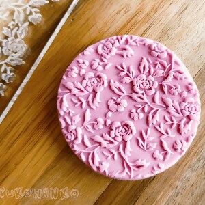 Op de afbeelding: Een roze siliconen cakedecoratiestempel met een bloemenpatroon. De stempel heeft een herhalend patroon van rozen en bladeren.