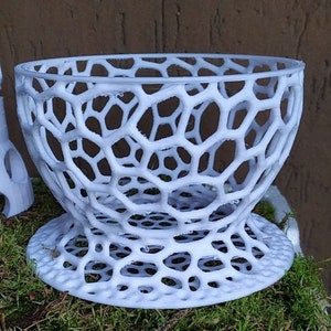 May include: A white, openwork bowl with a honeycomb-like design. The bowl has a wide, rounded top and a flared base. The intricate pattern creates a visually interesting texture. The bowl is likely made of plastic or a similar material.