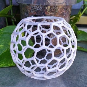 May include: White, 3D printed, geometric sphere with a honeycomb pattern. The sphere is hollow and has a round opening at the top.
