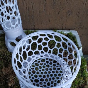 May include: White, open-weave decorative objects with a honeycomb pattern. The objects are placed on a bed of green moss. One object is cylindrical, and the other is bowl-shaped.