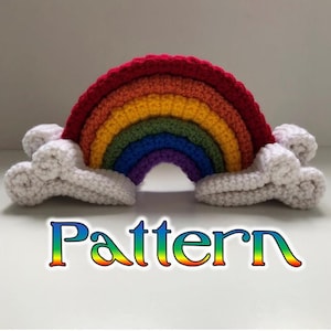 Puede incluir: Un arcoíris de crochet con nubes blancas a cada lado. El arcoíris está hecho de hilo rojo, naranja, amarillo, verde, azul, añil y violeta. La palabra "Pattern" está escrita en colores arcoíris debajo del arcoíris.